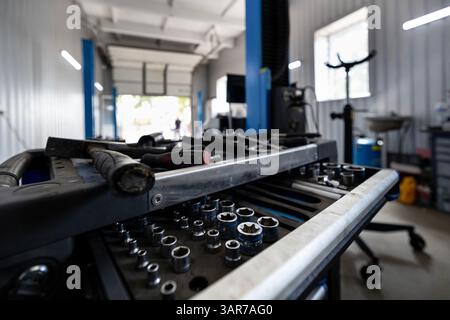 A rolling tool cart filled with sockets and various hand tools sits in a spacious auto repair shop with lifts and other equipment. Stock Photo