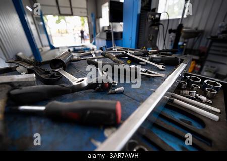 A rolling tool cart filled with sockets and various hand tools sits in a spacious auto repair shop with lifts and other equipment. Stock Photo