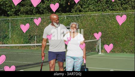 Image of pink hearts over smiling senior african american couple embracing outdoors after tennis Stock Photo
