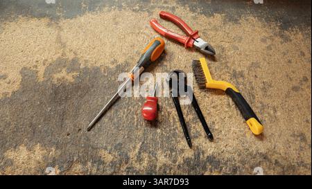 Hand tools including pliers, screwdriver, wire brush, and pincers lying on workbench in workshop Stock Photo