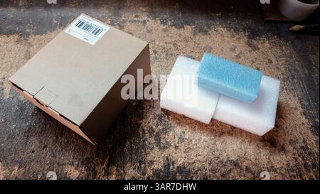 Cardboard shipping box and protective foam padding materials sit on a dusty workbench, suggesting packing or unpacking activities in a workshop enviro Stock Photo