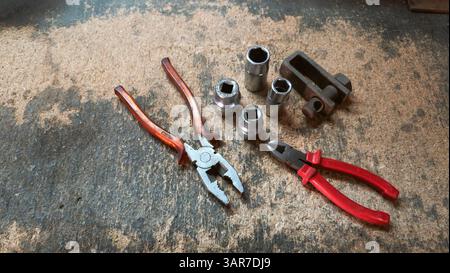 Combination pliers, diagonal cutting pliers and sockets resting on a workbench covered with sawdust and wood chips Stock Photo