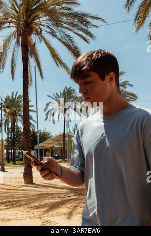 Tourist using mobile phone in a park with palm trees on a sunny day Stock Photo