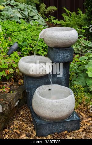 Cascading granite bowls water fountain in mulch border in backyard garden in summer. Stock Photo