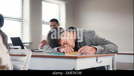Tired, school and boy in classroom at desk with fatigue for writing assignment, test and quiz. College, university and exhausted student sleeping for Stock Photo