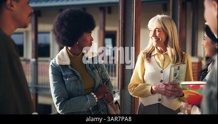 School, college and teacher with students talking in corridor greeting for learning, lesson and education. University, academy and lecturer with Stock Photo