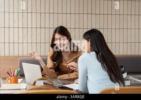 Collaboration and Creativity. Two students share ideas and knowledge while using a laptop in a shared study space. Stock Photo