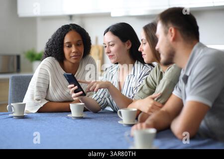Interracial friends using smart phone in the kitchen at home Stock Photo