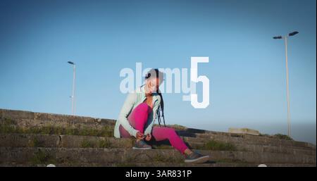 Number countdown against african american fit woman tying her shoe laces sitting on the stairs Stock Photo