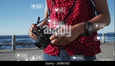 Multiple speech bubbles with digital icons against african american woman with a digital camera Stock Photo