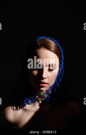 A young woman in a blue headscarf poses gracefully, her serene expression captivating all. Stock Photo