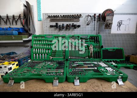 An open 216-piece flank socket wrench set is displayed on a workbench in a workshop, with various other tools organized on a pegboard in the backgroun Stock Photo