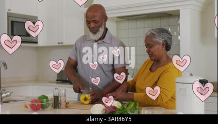 Image of pink hearts over happy african american senior couple preparing food in kitchen Stock Photo