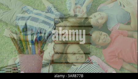 Image of books moving over happy school children lying on grass Stock Photo