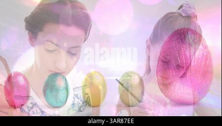 Image of easter eggs over caucasian mother and daughter decorating eggs Stock Photo