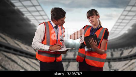 Image of stadium over caucasian male and female workers talking and using tablet Stock Photo