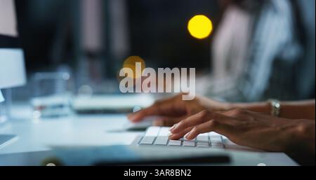 Person, hands and typing with keyboard at night for research, email or communication at office desk. Closeup, journalist or reporter working late on Stock Photo