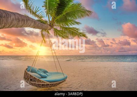 Relax sunset swing hammock on palm tree on tropical beach. Sun rays vibrant sky clouds. Honeymoon love couple island escape. Sea sand nature landscape Stock Photo