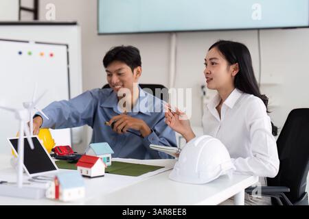 Engineering and Sustainability. Two engineers collaborating on an eco-friendly building project using model houses and renewable energy solutions. Stock Photo