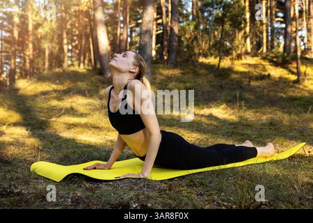 woman practicing yoga exercises on a mat in a sunny forest. stretching exercises Stock Photo