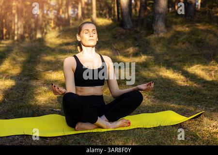 woman practicing yoga exercises and meditation on mat in a sunny forest. enjoying the beauty of mindfulness and nature Stock Photo