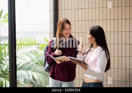 College Life and Academic Success. Two students engaging in a conversation while reviewing notes in an inspiring study environment. Stock Photo
