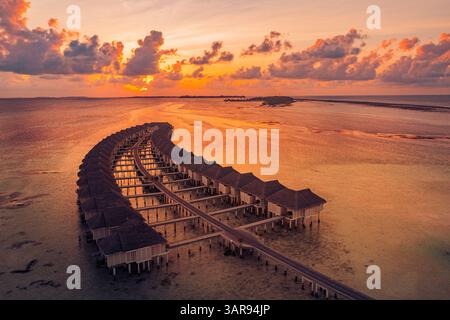 Aerial view of stunning Maldives water villas during a vibrant sunset, showcasing turquoise waters, tropical paradise, and serene island getaway vibes Stock Photo
