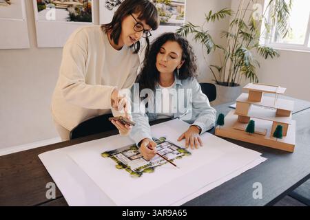 Architects reviewing draft plans while collaborating in a bright workspace featuring a wooden scale model. Stock Photo