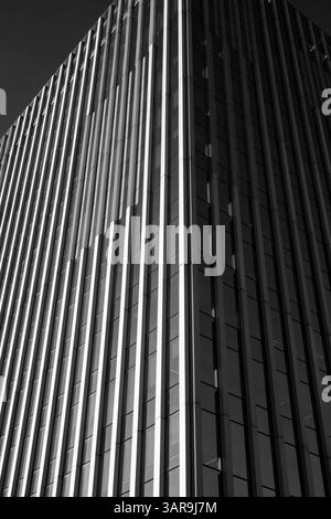 An impressive modern skyscraper reaches into a clear blue sky, showcasing architectural prowess and design. The building has sleek lines. Urban scene. Stock Photo