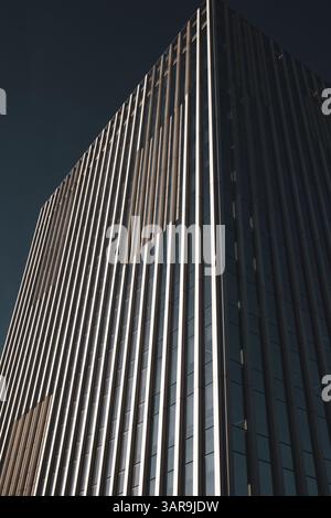 An impressive modern skyscraper reaches into a clear blue sky, showcasing architectural prowess and design. The building has sleek lines. Urban scene. Stock Photo