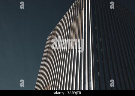 An impressive modern skyscraper reaches into a clear blue sky, showcasing architectural prowess and design. The building has sleek lines. Urban scene. Stock Photo