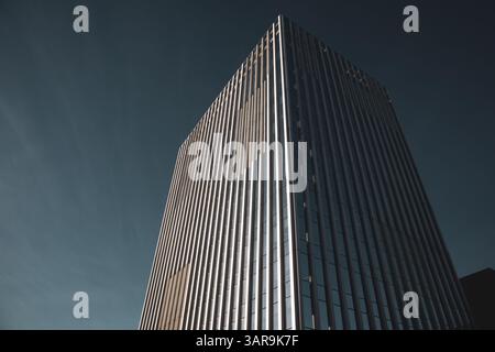 An impressive modern skyscraper reaches into a clear blue sky, showcasing architectural prowess and design. The building has sleek lines. Urban scene. Stock Photo