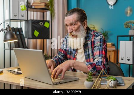 Frustrated senior man having software problems with laptop, angry man get nervous seeing error or mistake notification at computer screen, mad grandpa experience virus attack or app malfunction. Stock Photo