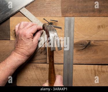 Caucasian man's hands hammering nail on rough wood background with assorted hand tools Stock Photo