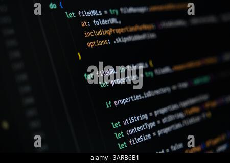 Close-up of Swift programming code on dark screen displaying loop and conditional logic for file management, reading file properties like size, type, Stock Photo