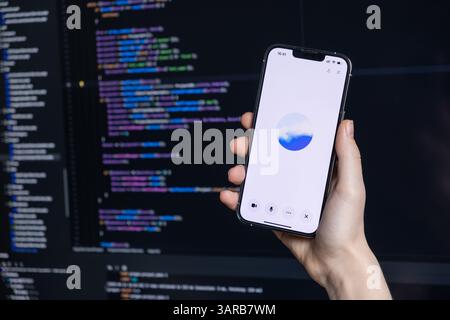 Poznan, Poland – April 14, 2025: Person holding smartphone with ChatGPT voice interface open while coding on computer, showing AI integration in moder Stock Photo