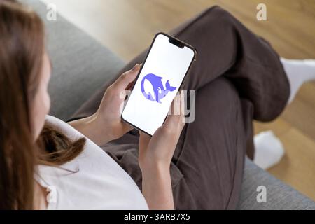 Poznan, Poland – April 14, 2025: Female user sitting comfortably on sofa holding smartphone with DeepSeek AI logo, exploring artificial intelligence a Stock Photo