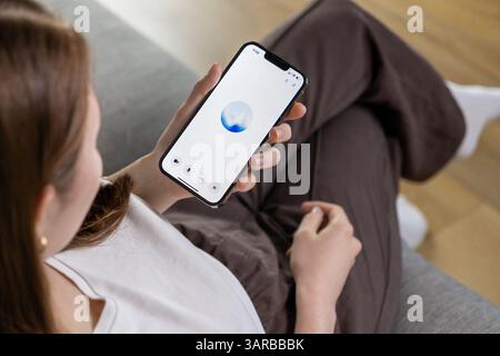 Poznan, Poland – April 14, 2025: A woman interacts with an AI assistant through voice input on her phone, displaying a blue animated circle on a minim Stock Photo