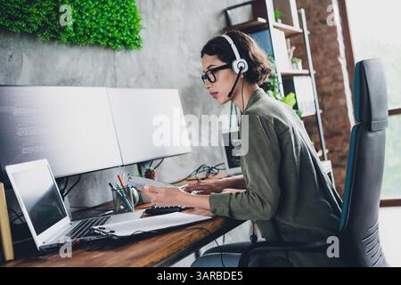 Young female programmer working remotely in a stylish home office with dual monitors, coding software and managing tasks efficiently Stock Photo