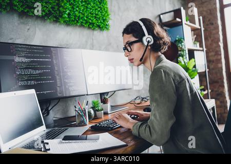 Young female programmer working remotely from stylish workspace with multiple monitors and casual attire Stock Photo