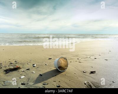 Plastic cup lies discarded on a sandy beach, polluting the environment and posing a threat to marine life Stock Photo