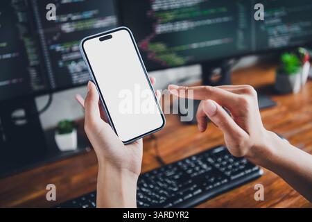 Young female software developer using smartphone for coding in modern workspace with computer screens and programming tools Stock Photo