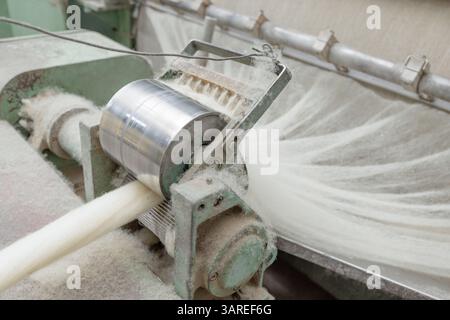 Raw wool fibers being processed through a carding machine in a textile mill, preparing material for spinning. Stock Photo