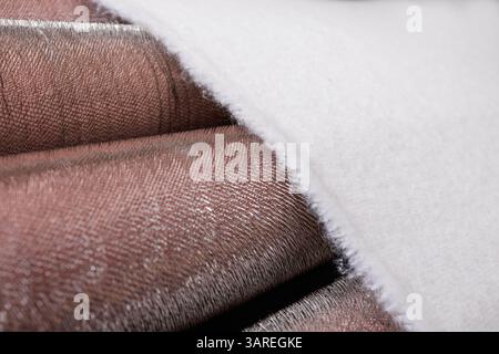 Close-up of white fabric moving through metal carding rollers during the textile manufacturing process. Stock Photo