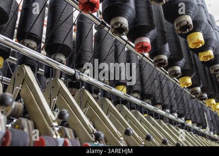 Black yarn spools spinning on an automated textile machine in a modern factory during fabric production. Stock Photo