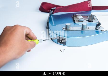 Close-up of a hand using a screwdriver to repair or install the input jack on an electric guitar. Ideal for music, maintenance, or DIY-themed content. Stock Photo