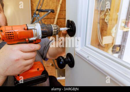 Contractor carefully installs black door handle lock using power drill in home setting. Stock Photo
