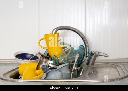 Dirty and unwashed dishes are stacked in the kitchen sink. Unwashed cups, plates, pots, forks and spoons.A mountain of untidy and used dishes Stock Photo