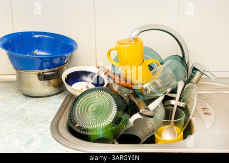 Dirty and unwashed dishes are stacked in the kitchen sink. Unwashed cups, plates, pots, forks and spoons.A mountain of untidy and used dishes Stock Photo