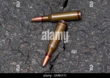 Two cartridges with a bullet with an offset center lies on a dark textural background, selective focus, Concept:prohibited expansive bullets, the war Stock Photo